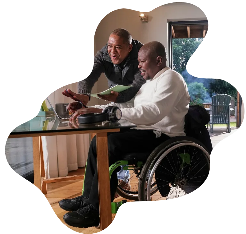 Disabled man in wheelchair at home using laptop with support worker