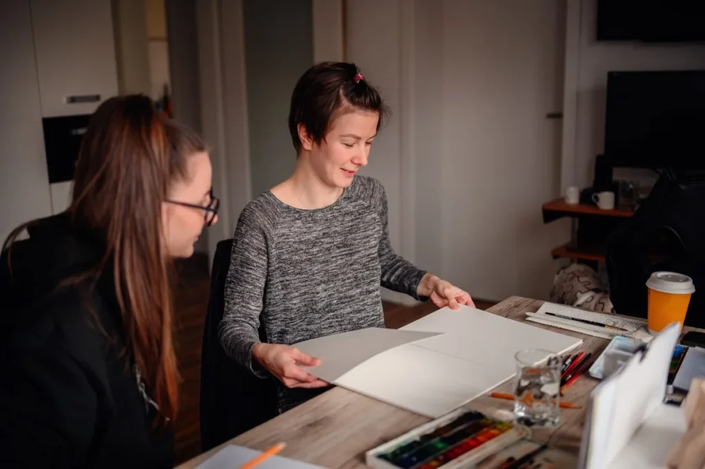 Support worker helping disabled girl draw in her art book